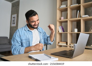 Overjoyed Happy Indian Latin Guy, Lucky Winner, Sitting At Desk Watching Virtual Lottery Results On Laptop Shacking Hands. Eastern Student Got Perfect Exam Grades, Job Proposal Offer.