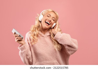 Overjoyed happy lady with headphones and smartphone listening to music and dancing, enjoying cool playlist and moving to favorite song over pink background - Shutterstock ID 2122515785