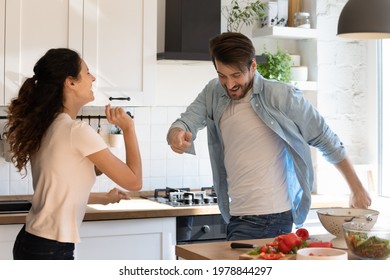 Overjoyed Happy Laughing Sincere Young Family Couple Dancing To Music, Enjoying Domestic Entertainment Activity In Modern Kitchen, Preparing Together For Party, Having Fun On Weekend At Home.