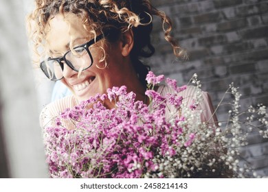 Overjoyed happy woman smiling and hugging a floreal flowers bouquet at home with joyful expression. Concept of anniversary or birthday. Love and relationship present couple. Excited female people - Powered by Shutterstock