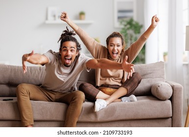 Overjoyed happy young african american couple man and woman raising arms, celebrating goal and screaming while watching football match together at home, selective focus. Leisure weekend activities - Powered by Shutterstock