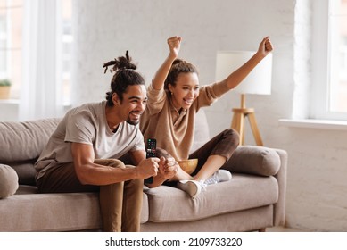 Overjoyed happy young african american couple man and woman raising arms, celebrating goal and screaming while watching football match together at home, selective focus. Leisure weekend activities - Shutterstock ID 2109733220