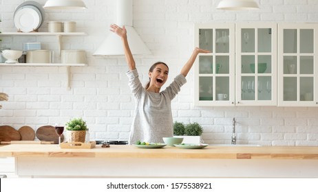 Overjoyed Happy Young Woman Raise Hands Feel Excited Cooking Alone In Modern Kitchen Interior, Funny Independent Girl Dancing Prepare Dinner At Home Having Fun Enjoy Freedom Healthy Lifestyle Concept