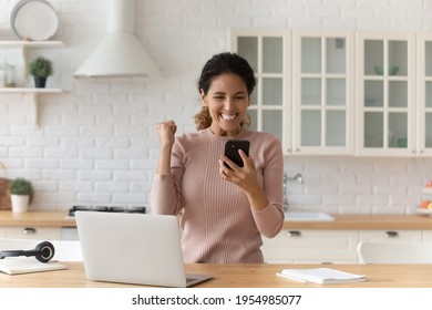 Overjoyed hispanic woman student on distant learning receive text message on cell with good exam results. Happy female freelancer celebrate getting money reward positive feedback for work from client