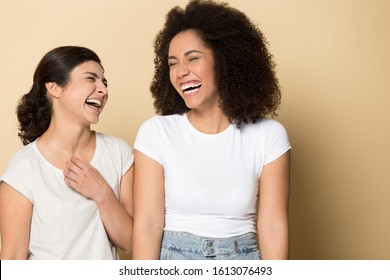 Overjoyed indian and african american ethnic young girls communicating, telling jokes, laughing at funny stories, feeling joyful and happy head shot portrait, isolated on yellow studio background.