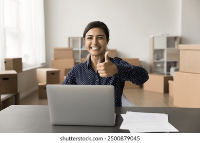 Overjoyed Indian businesswoman, individual entrepreneur, small business owner celebrates first sale, smile look at camera showing thumb up gesture, working in warehouse with cardboard boxes. Success - Powered by Shutterstock