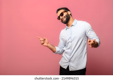 Overjoyed Indian man wearing sunglasses dancing, makes movements to music, smiles positively, being in high spirit. Carefree hispanic guy in blue jeans shirt dances isolated on pink - Shutterstock ID 2149896315