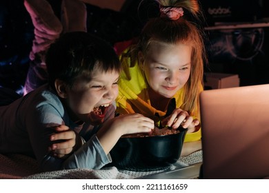 Overjoyed Kids Sister Brother Laughing Spend Weekend Free Time Together At Home On Couch Bed Eating Popcorn. Teen Children Watching Video Cartoon Use Remote Control On Laptop Have Fun. Movie Night