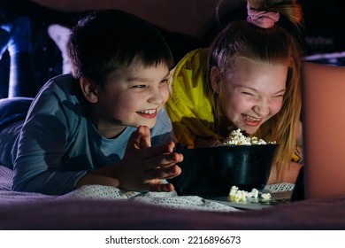 Overjoyed Kids Sister Brother Laughing Spend Weekend Free Time Together At Home On Couch Bed Eating Popcorn. Teen Children Watching Video Cartoon Use Remote Control On Laptop Have Fun. Movie Night