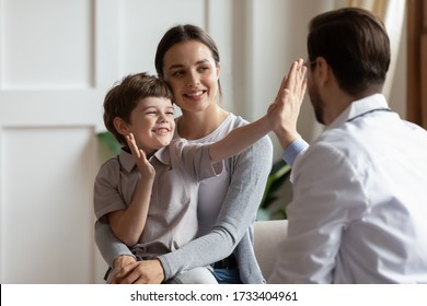 Overjoyed Little Boy Patient Have Fun Give High Five To Male Doctor At Consultation In Clinic With Mom, Happy Small Child Greeting With Man Pediatrician At Checkup In Hospital, Healthcare Concept