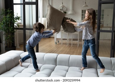 Overjoyed little sister and brother siblings pillow fighting, jumping on cozy couch at home, happy smiling girl and boy having fun, engaged in funny activity, spending leisure time together - Powered by Shutterstock