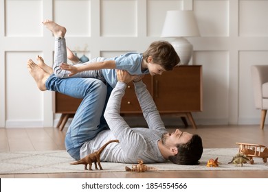 Overjoyed loving father playing active game with adorable son, lying on warm floor at home, happy dad holding carrying little boy with hands outstretched pretending flying, enjoying leisure time - Shutterstock ID 1854554566