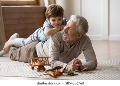 Overjoyed Mature Grandfather Playing With Adorable Grandson At Home, Older Man Lying On Warm Floor With Cute Little Boy Grandchild On Back, Family Spending Leisure Time Together, Having Fun