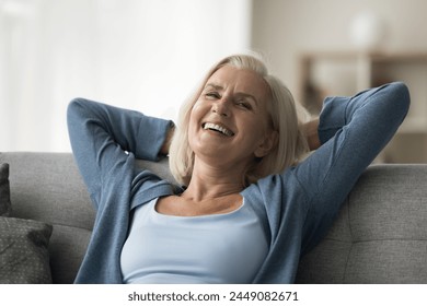 Overjoyed mature woman lounging on cozy sofa, laugh, look at camera, enjoy relaxation leaned on comfortable couch in living room alone at own or rented flat. Carefree retirement, stress-free leisure - Powered by Shutterstock