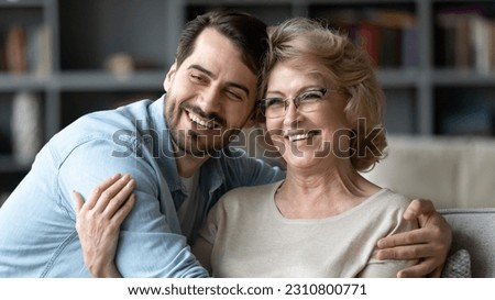 Overjoyed mature woman wearing glasses and adult son hugging, posing for photo, hugging, sitting on couch in living room, excited happy middle aged mother and young man embracing, two generations Stock photo © 