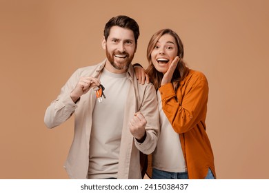 Overjoyed middle aged couple holding keys from new home isolated on beige background. Happy man and woman buying a house looking at camera, celebration success - Powered by Shutterstock