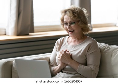 Overjoyed middle-aged woman in glasses sit on couch in living room triumph reading good news on laptop, happy excited senior female feel euphoric win online lottery on computer, luck concept