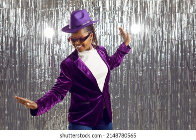 Overjoyed millennial African American girl in party jacket and hat dance on glitter studio background. Happy young black woman in costume and glasses have fun. Entertainment concept. - Powered by Shutterstock