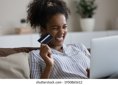 Overjoyed millennial African American woman have fun shopping online with credit card on laptop. Excited young biracial female buy pay on internet on computer at home use good banking secure system.