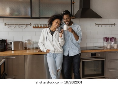 Overjoyed millennial biracial family man and woman relax drink coffee together in new renovated home kitchen. Happy young African American couple renters enjoy moving relocation to own house. - Powered by Shutterstock