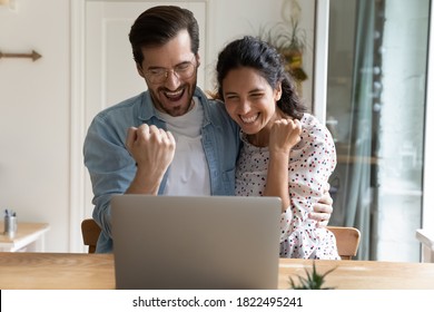 Overjoyed Millennial Caucasian Couple Look At Screen Triumph Winning Online Lottery On Laptop. Happy Young Man And Woman Feel Euphoric Read Good News On Computer, Excited With Sale Deal Or Offer.