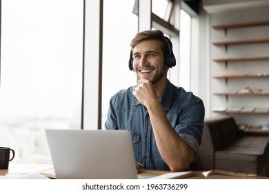 Overjoyed Millennial Caucasian Male Employee In Headphones Work Online On Laptop Talk With Colleague Coworker. Smiling Young Man In Earphones Have Webcam Video Call. Virtual Event Concept.