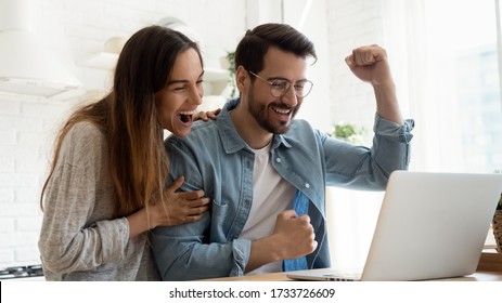 Overjoyed millennial couple sit at desk look at laptop screen feel euphoric with online win, excited happy young husband and wife read good news, get unexpected notification on computer, luck concept - Shutterstock ID 1733726609