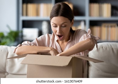 Overjoyed millennial girl sit on sofa in living room unpack cardboard parcel with online Internet order, happy young woman client customer open carton box shopping on Web, good delivery concept