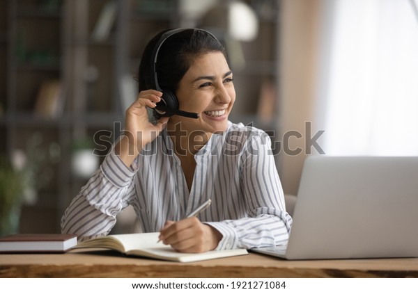 Overjoyed\
millennial Indian woman in earphones study online on laptop take\
notes. Happy young mixed race female in headphones work distant on\
computer. Education, virtual event\
concept.