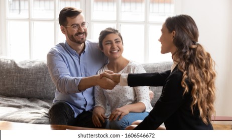 Overjoyed Millennial International Couple Handshake Female Banker Or Broker Get Acquainted At Meeting, Smiling Multiethnic Young Husband And Wife Shake Hands Greeting Or Closing Deal With Realtor