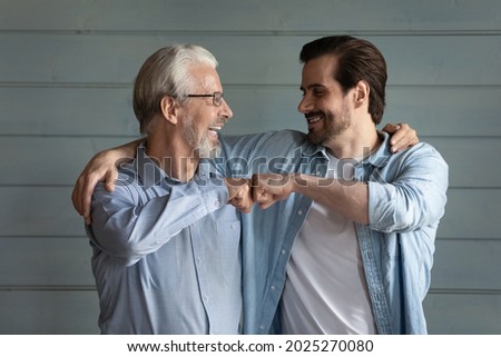 Overjoyed millennial man child and old Caucasian father isolate don grey wall background celebrate win or victory. Happy adult grownup son and mature dad give fist bump show unity and support. Stock photo © 