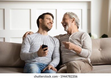 Overjoyed millennial man and senior father relax on sofa at home laugh watching funny video on cellphone together. Smiling old Caucasian dad and adult grownup son have fun using smartphone device. - Powered by Shutterstock