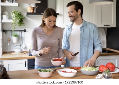 Overjoyed Millennial Man And Woman Have Fun Cooking Healthy Tasty Vegetarian Salad In Kitchen Together. Smiling Young Caucasian Couple Prepare Delicious Vegetable Diet Food In Own Cozy House.