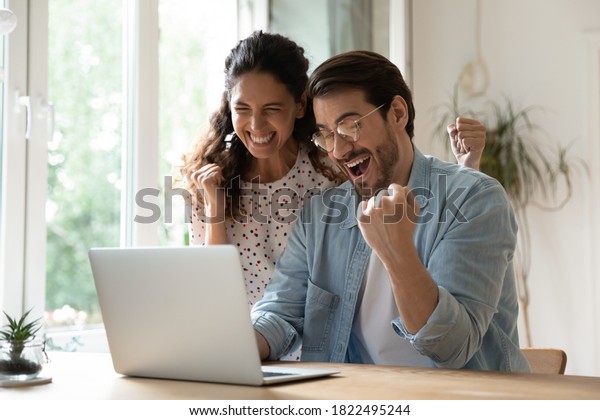Overjoyed millennial man and woman triumph win\
online lottery on laptop. Happy excited young Caucasian couple feel\
euphoric with good email, get amazing sale offer or discount deal\
on computer.