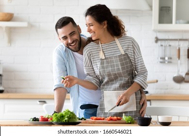 Overjoyed Millennial Vegetarian Couple Stand At Kitchen Counter Cooking Salad For Dinner Together, Happy Young Husband And Wife Chop Vegetables Preparing Food Or Lunch At Home, Dieting Concept