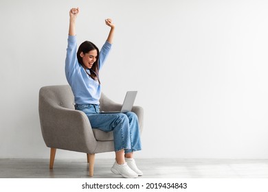 Overjoyed millennial woman sitting in armchair with laptop, celebrating huge online win or success against white studio wall, copy space. Young lady enjoying big sale in web store - Shutterstock ID 2019434843
