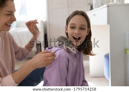 Overjoyed mother and teenage daughter having fun, playing with cute rat, family enjoying leisure time with pet together, little curious rodent sitting on laughing teen girl shoulder