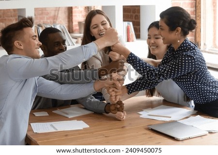 Overjoyed motivated multiracial young people join stack fists showing unity, support and teamwork spirit, smiling multiethnic students involved in teambuilding activity at group meeting in classroom