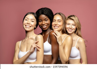 Overjoyed Multi Ethnic Group Of Womans With Diffrent Types Of Skin Standing Together And Looking On Camera. Diverse Ethnicity Women - Caucasian, African And Asian Against Pink Background