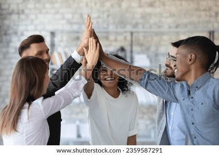 Overjoyed multiethnic businesspeople give high five engaged in teambuilding activity at meeting, happy diverse colleagues join hands celebrate shared victory or win at team briefing, success concept