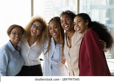Overjoyed multiethnic diverse female colleagues hug pose for team self-portrait picture together in office. Smiling multiracial women employees make selfie at workplace. Teamwork, success concept.