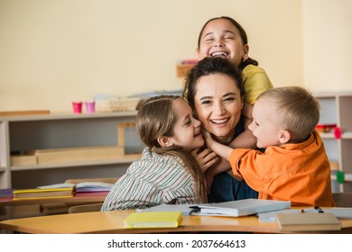 overjoyed multiethnic kids embracing happy teacher in montessori school
