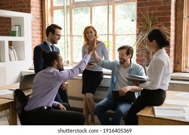 Overjoyed multiethnic male employees give high five motivated shared work success or promotion at meeting. Smiling multiracial men colleagues celebrate good job results engaged in office briefing. - Shutterstock ID 1916405369