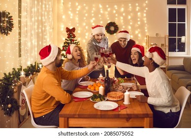 Overjoyed multiethnic people in Santa hats clink glasses dining together at table on Christmas eve. Smiling diverse friends cheers celebrate New Year winter holiday have delicious dinner at home. - Powered by Shutterstock