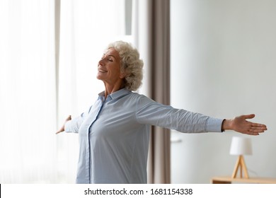 Overjoyed Old Woman Stretch Hands Feel Positive Optimistic About New Sunny Day At Home, Excited Smiling Mature Female Relax In Living Room Show Good Mood, Happy Elderly Lifestyle Concept