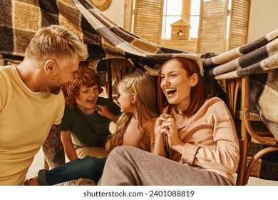 overjoyed parents laughing under blanket hut while playing with kids in living room, bonding moments - Powered by Shutterstock