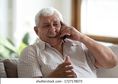 Overjoyed senior 80s grandfather sit on sofa at home laugh talking on modern cellphone, happy mature 70s man relax in living room speak have pleasant smartphone call, elderly and technology concept