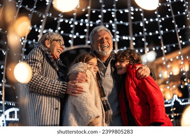 Overjoyed senior couple having fun with granddaughter and grandson surrounded with Christmas lights during winter holidays. - Powered by Shutterstock