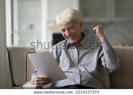 Overjoyed senior man sitting on sofa with papers, reading letter feels excited by good fantastic news received, get social pension growth, bank notification about loan repayment, money refund, profit