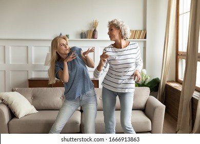 Overjoyed senior mother and adult daughter have fun enjoying family weekend at home together, happy mature mom and grownup millennial girl child dancing in living room, feel excited and optimistic